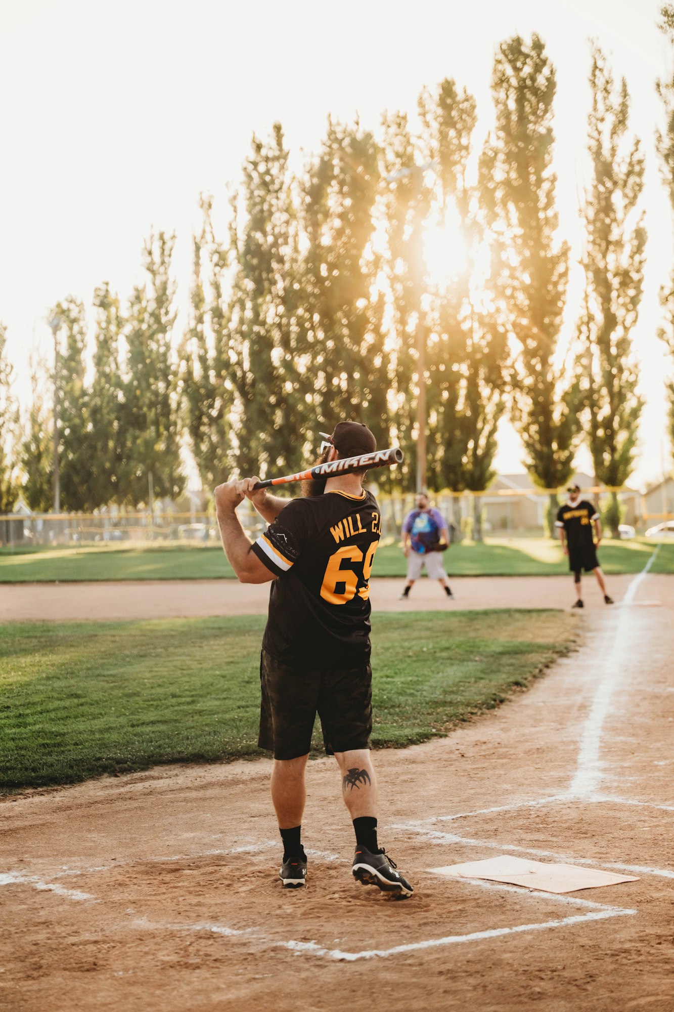 A batter prepares to swing at a softball game during sunset.