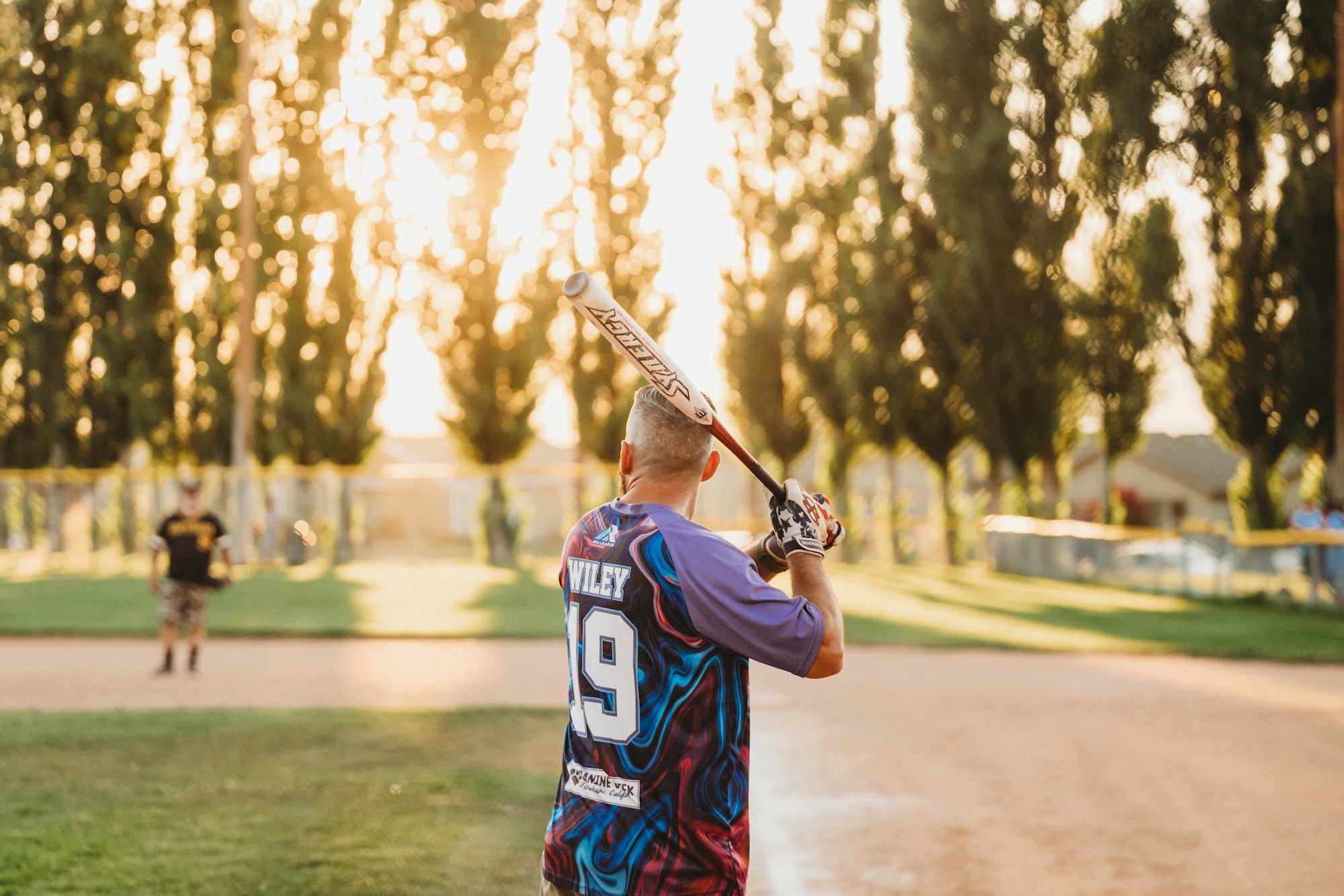 A baseball player holding a bat on the field at sunset.