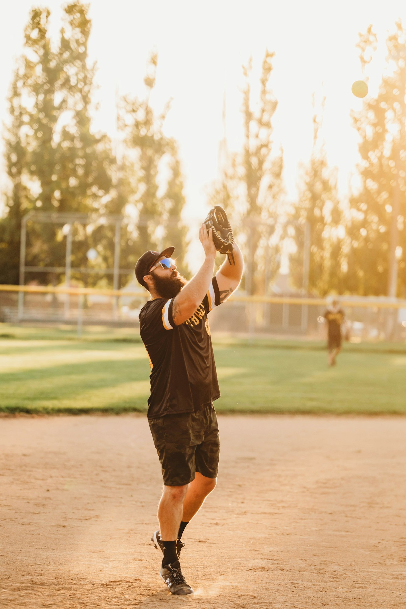 Man with glove catching a ball, playing baseball on a sunny day.