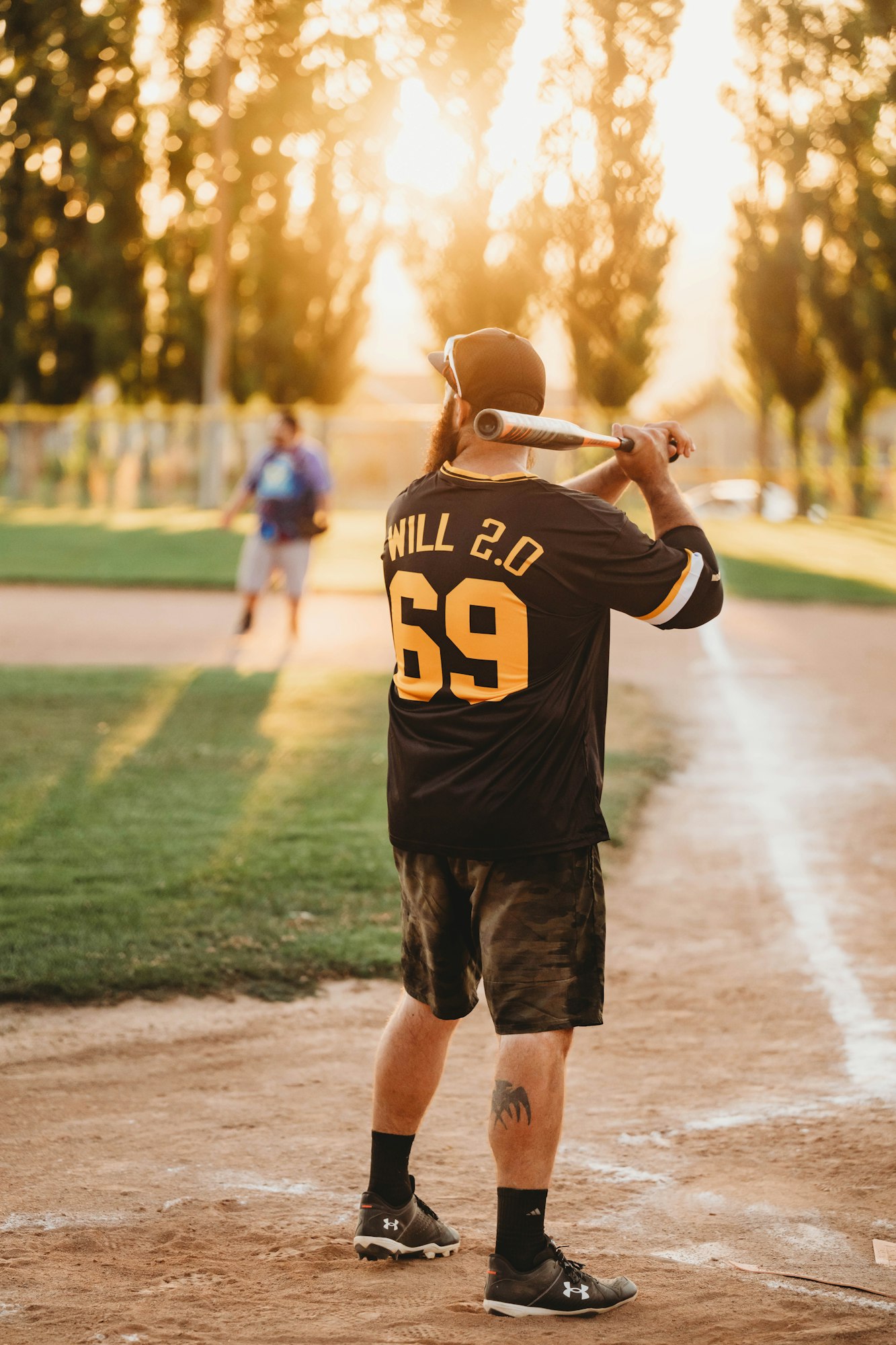 A person in a sports jersey and cap holding a baseball bat on a field, bathed in soft sunset light.