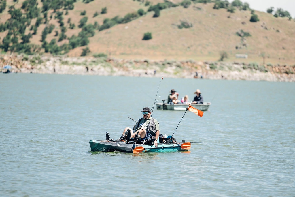 People on kayaks fishing in a lake with a hilly backdrop.