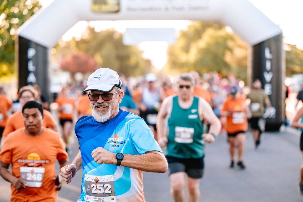 People running in a race, passing under an inflatable arch with race bib numbers.