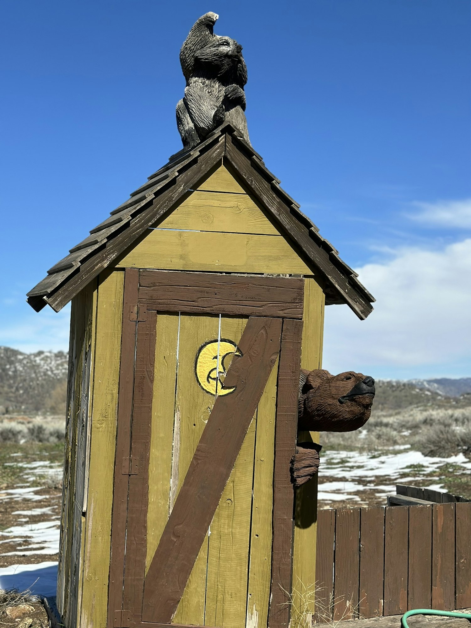 Wooden outhouse with bear sculptures, under blue sky.