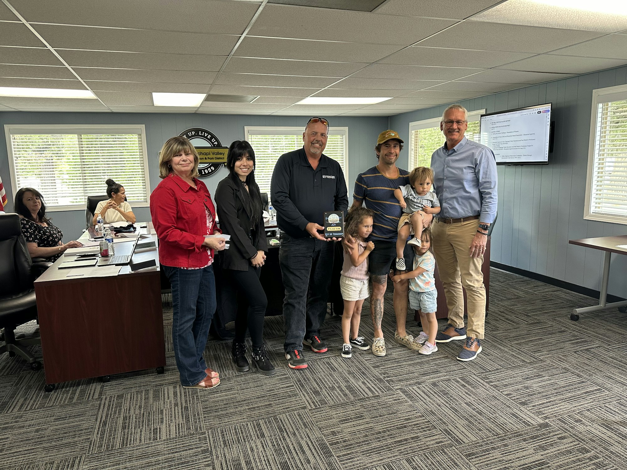 Individual receiving an award in a room with others, including two adults with three kids.