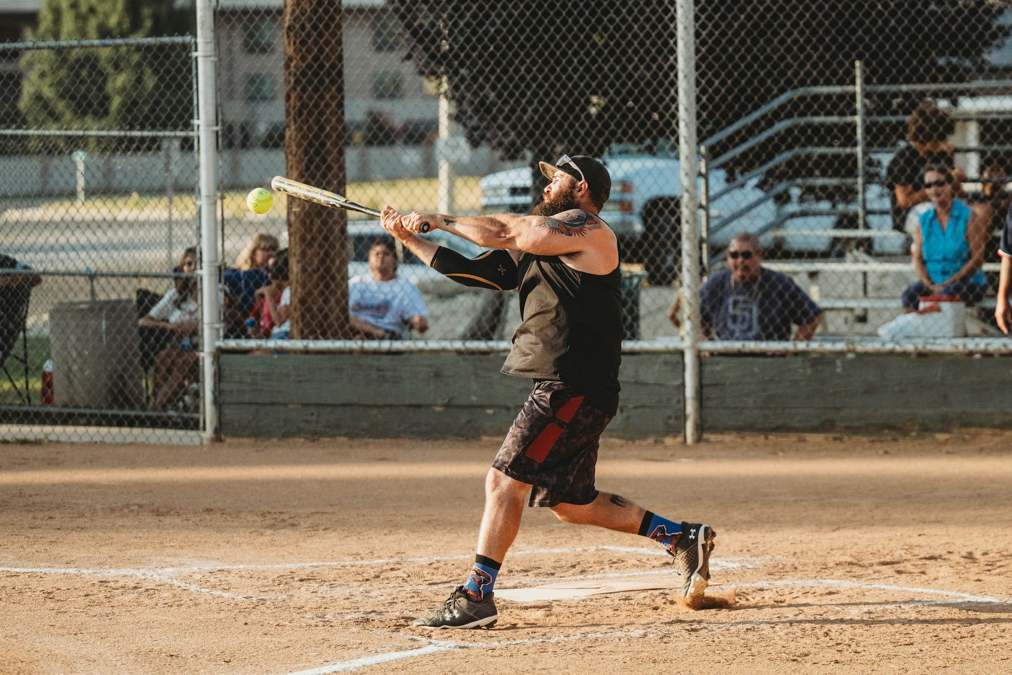 A person swinging a bat at a softball, with spectators in the background.