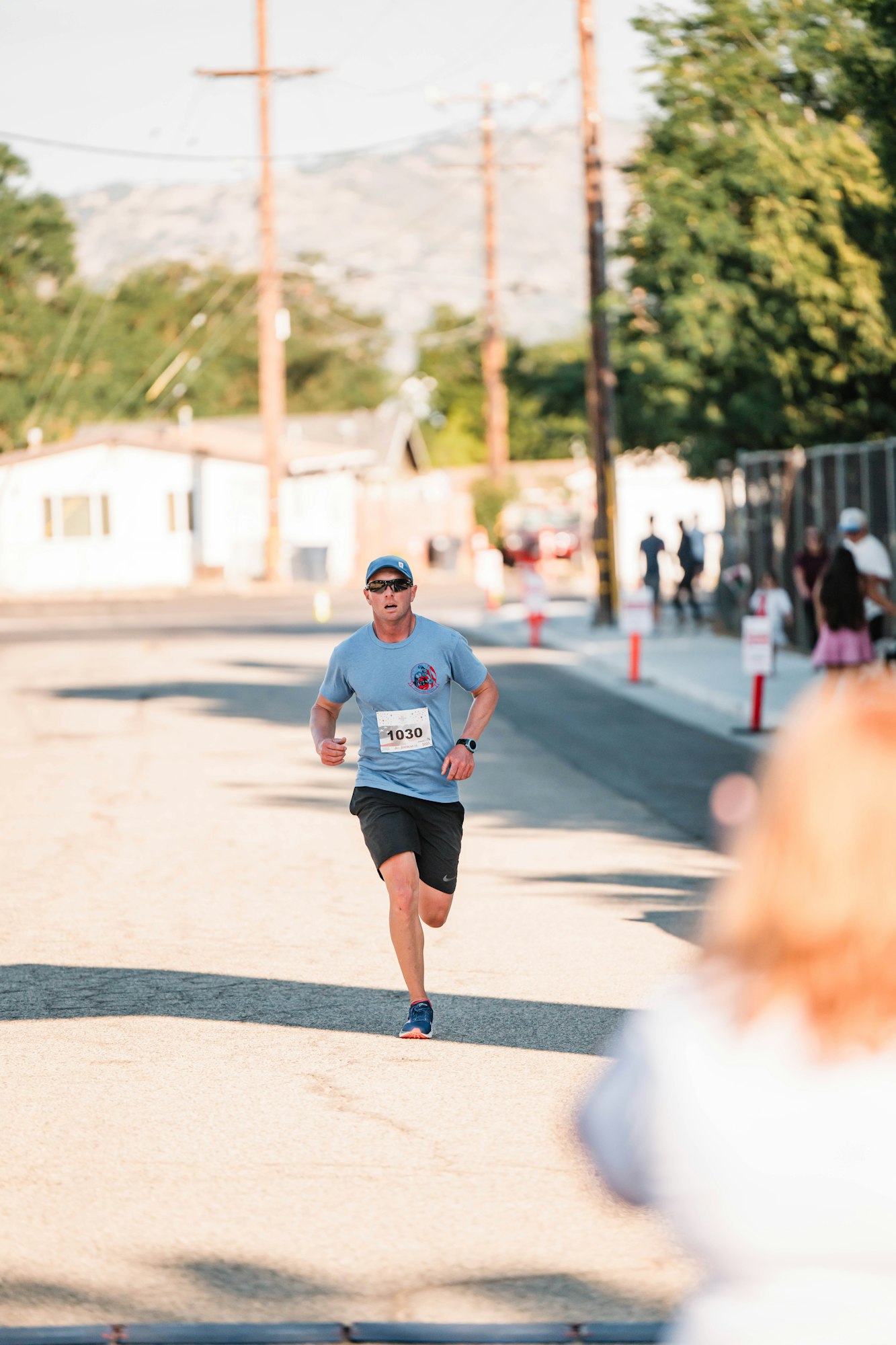 A person running on a street with a race bib, surrounded by trees and buildings.