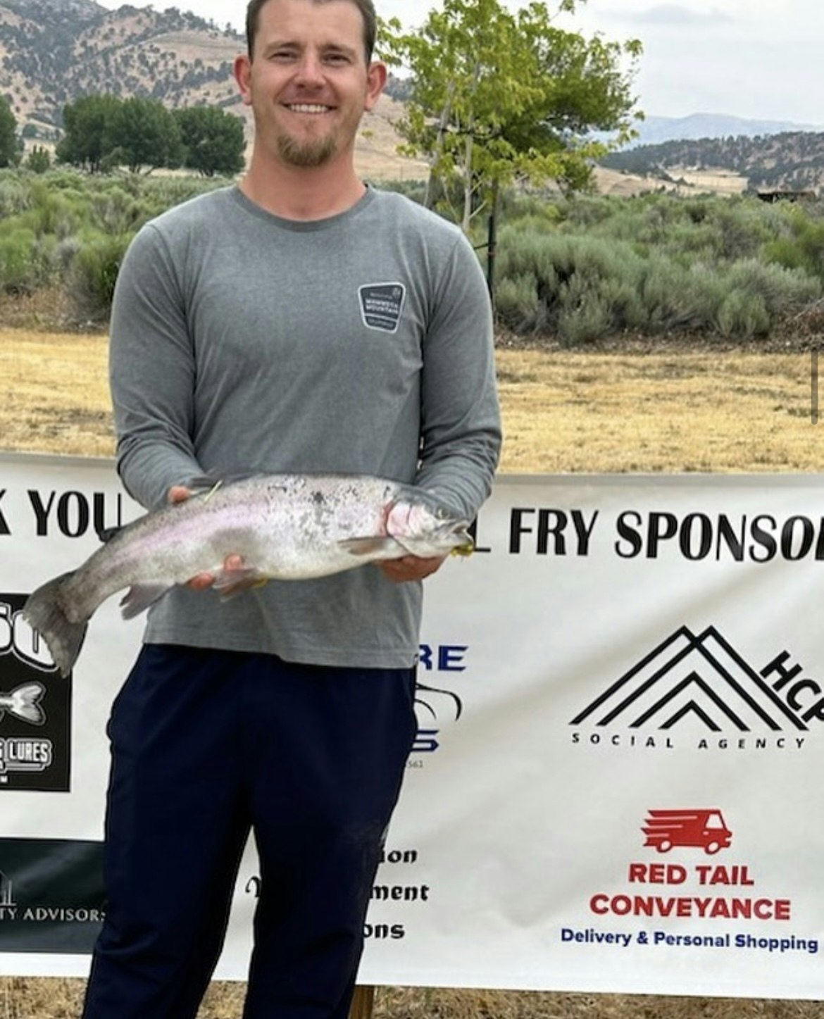 A man proudly holding a large fish with sponsor banners in the background.