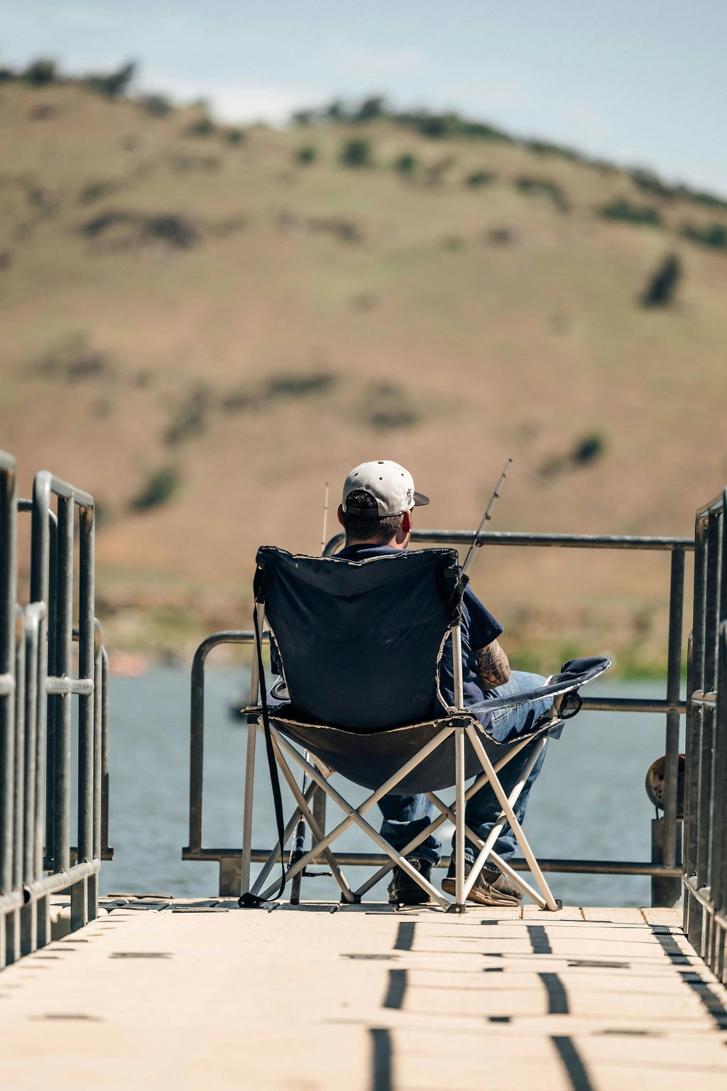 Person fishing from a jetty, hills in the background.