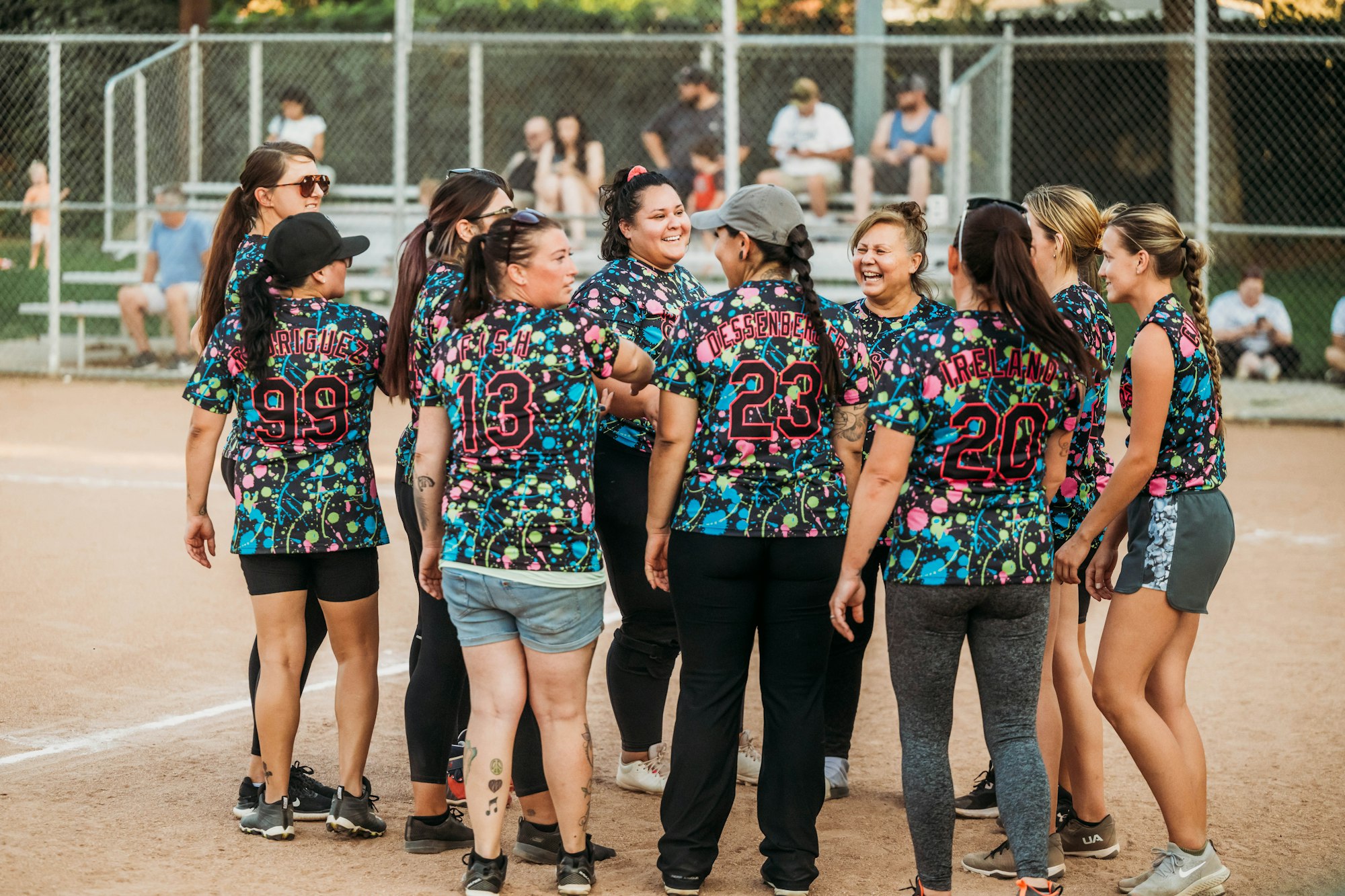 A group of cheerful softball players in colorful jerseys celebrating on a dirt field.