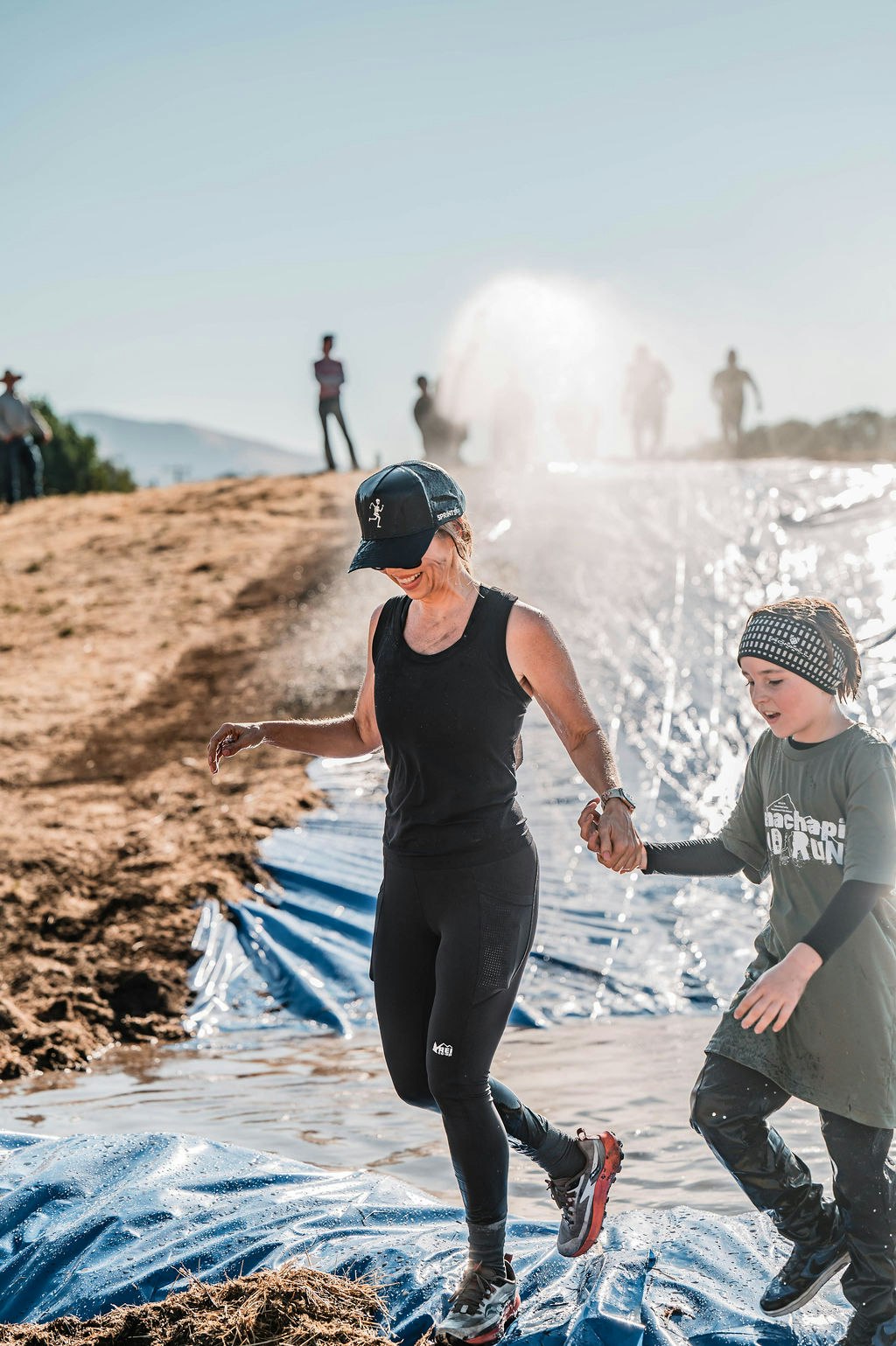 Two people holding hands, running on a wet slide with others in the background.