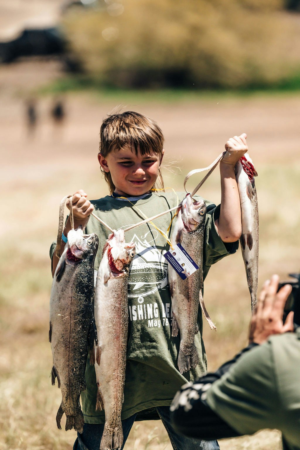 A happy child holding up several fish, possibly showing them off, with a person's hand visible in the foreground.