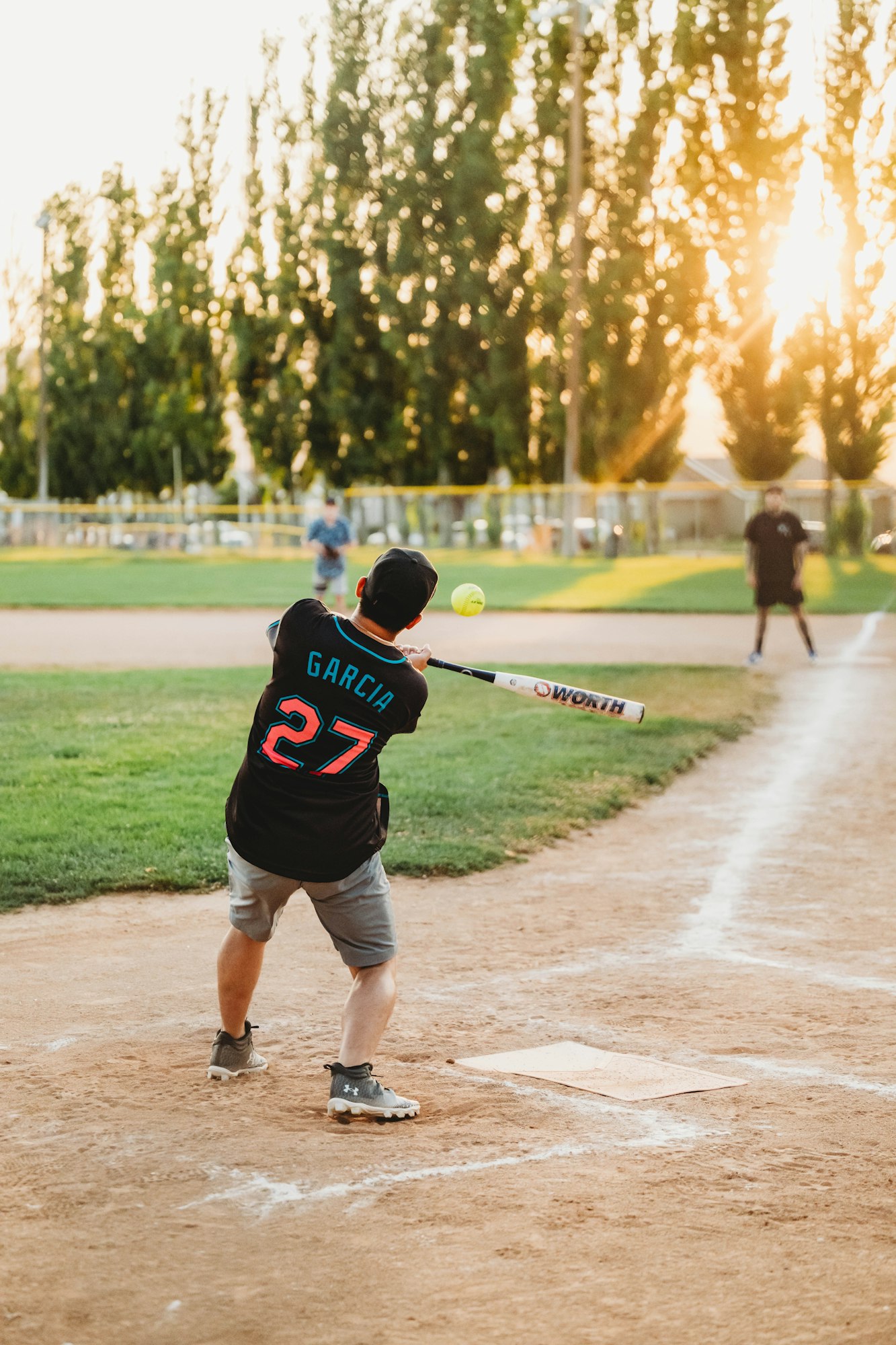 Player hitting a softball at sunset on a baseball field.