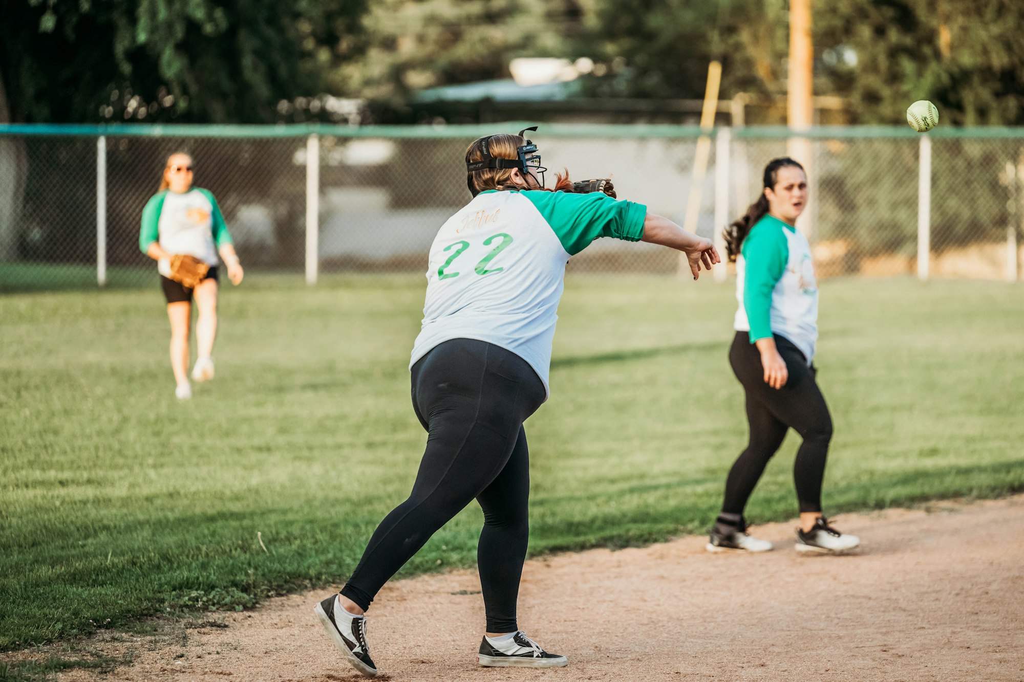 A softball game in action with one player throwing the ball and teammates in the background.