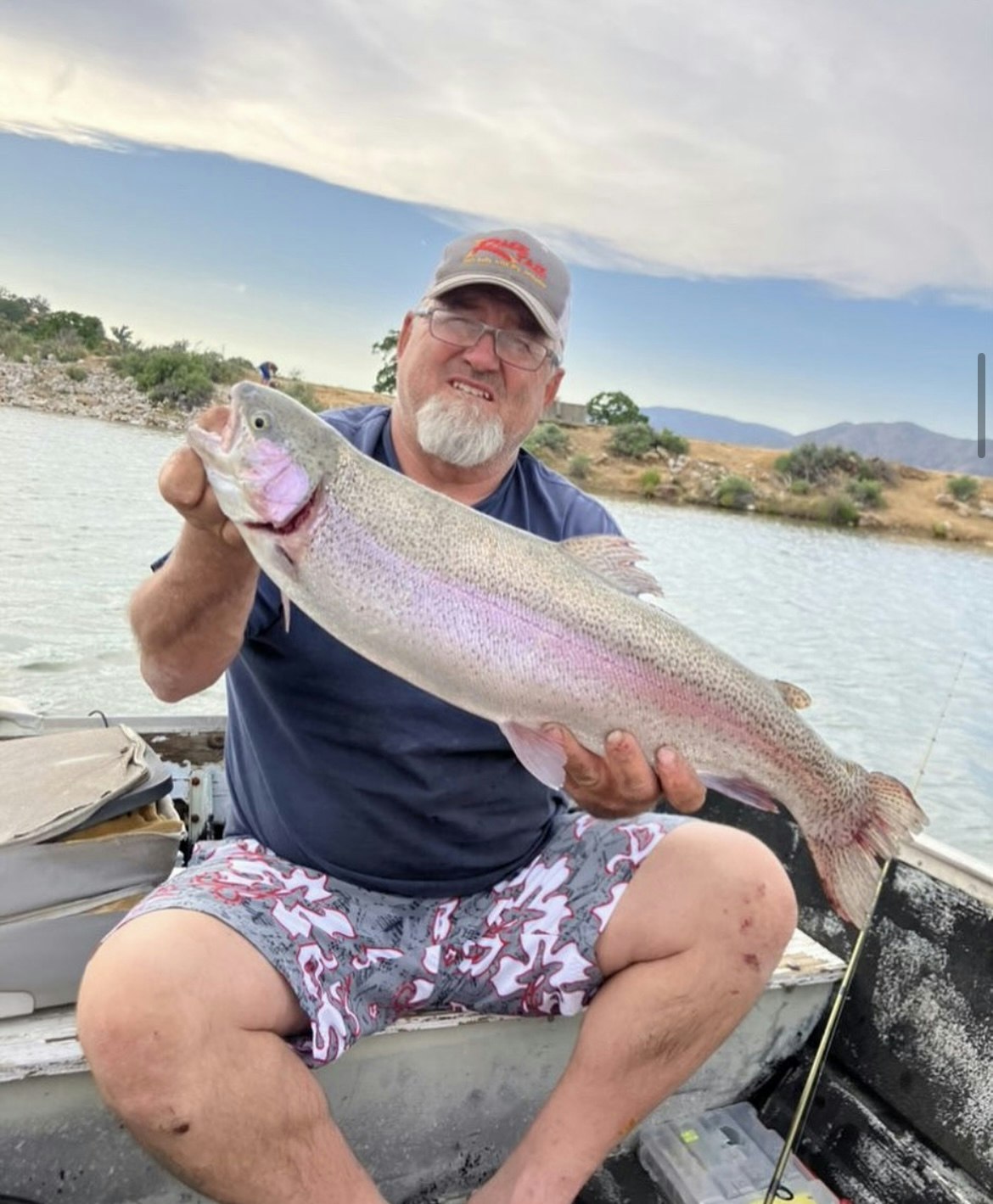 A man proudly holding a large fish in a boat on a river.