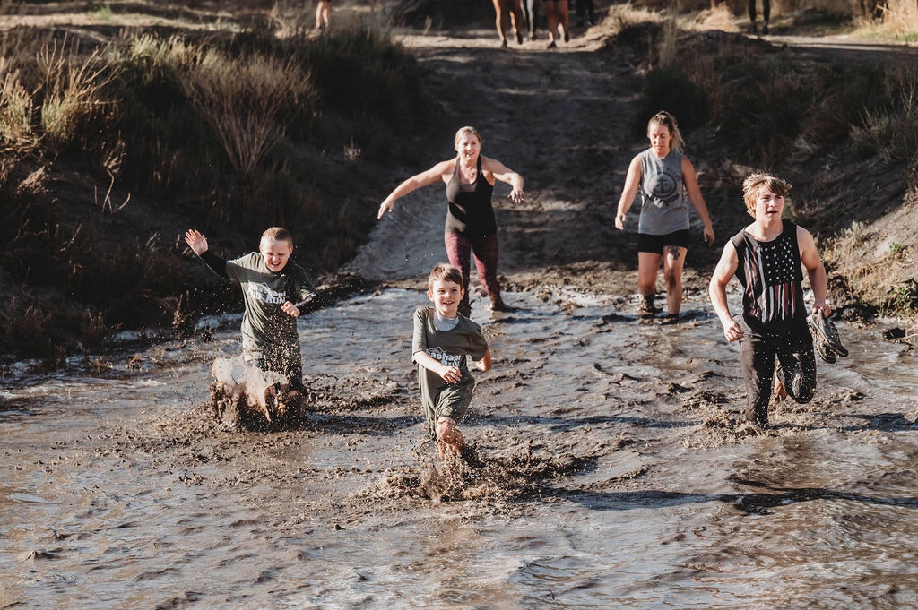 A group of people running through a muddy terrain, laughing and having fun.