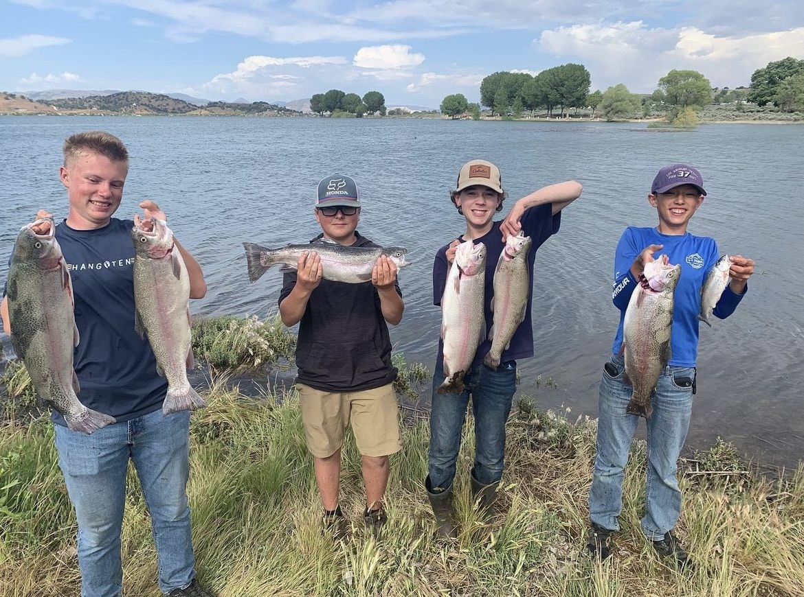 Four boys by a lake holding up their fish catches.