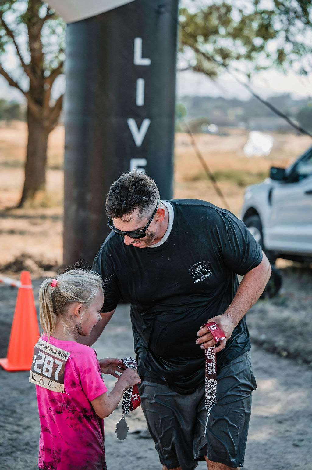 A man and a girl at an outdoor event, wearing sport clothes, exchanging medals.