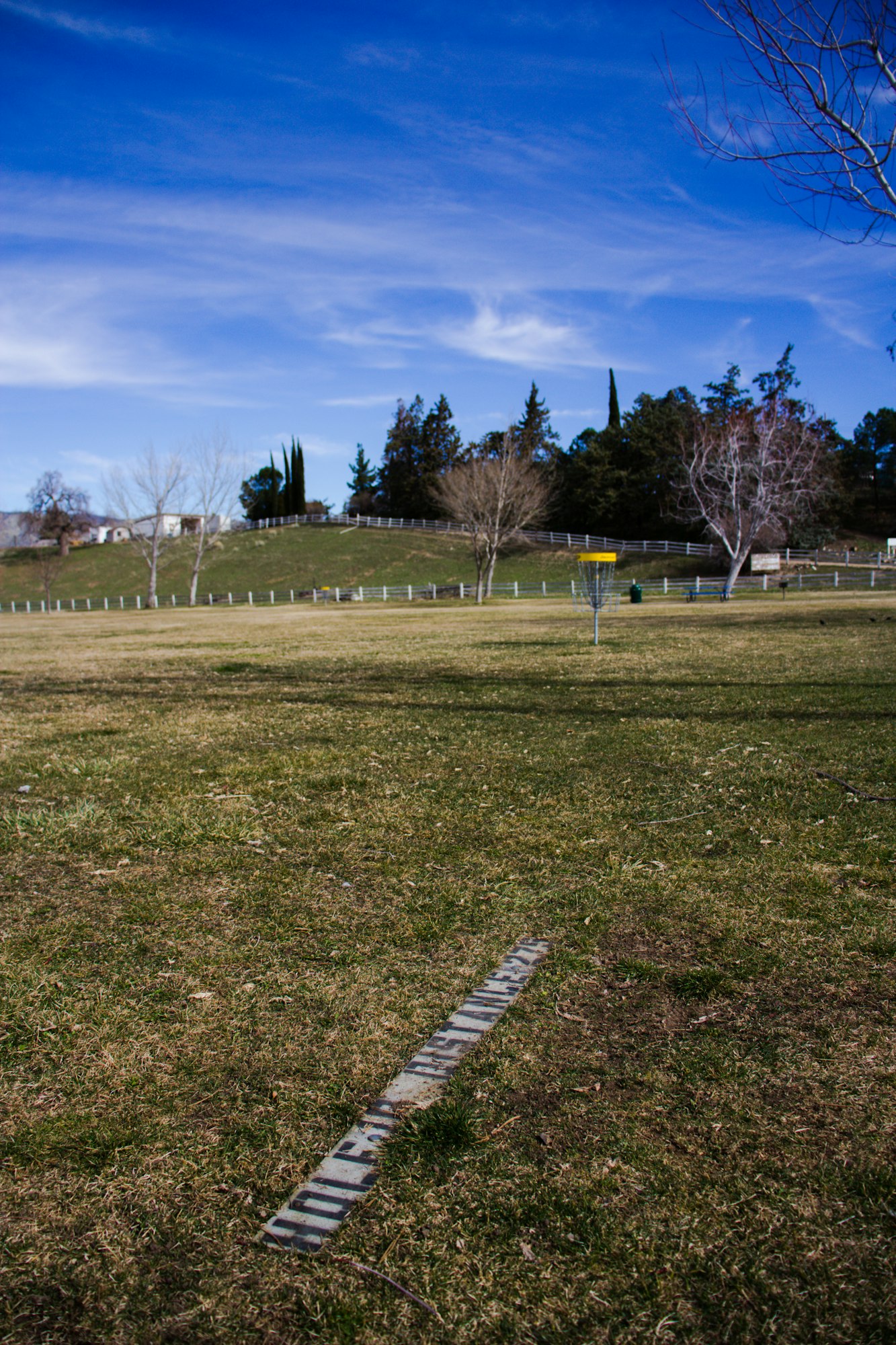 A disc golf basket in a park with clear skies and a launching pad on grass.