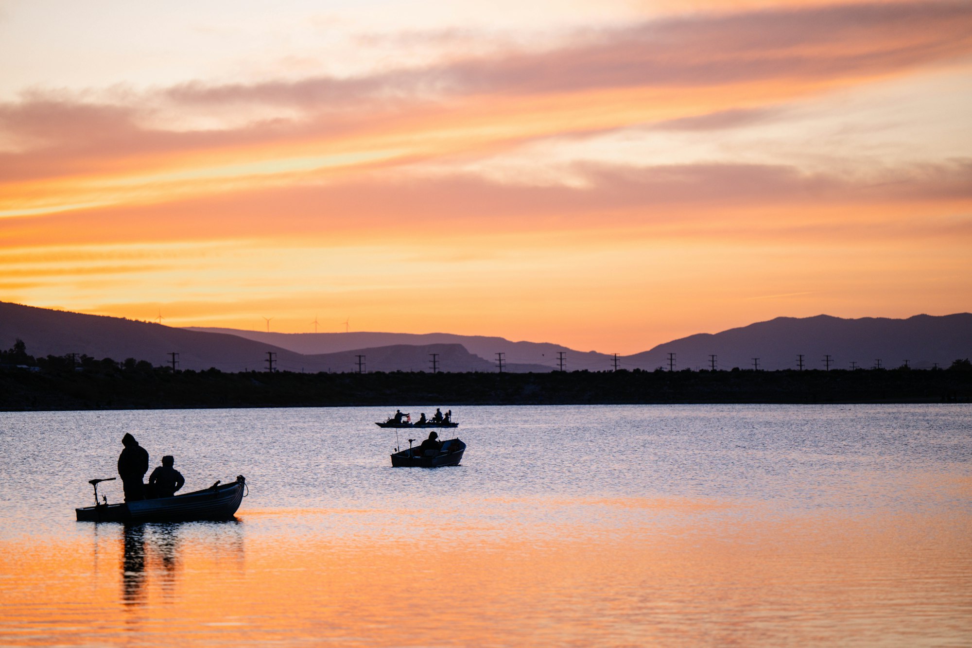 Boats on a calm lake at sunset with silhouetted figures and colorful sky.