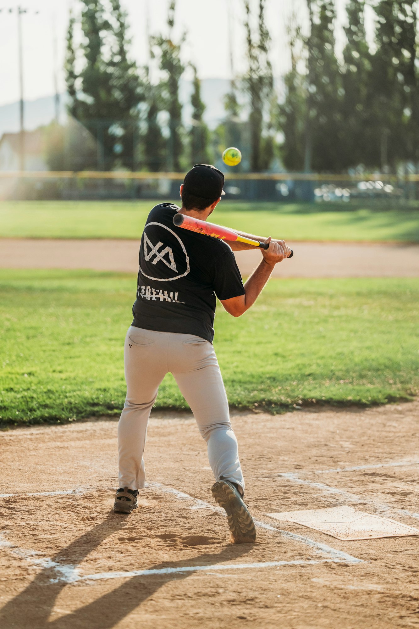 A batter hitting a softball on a sunny field.