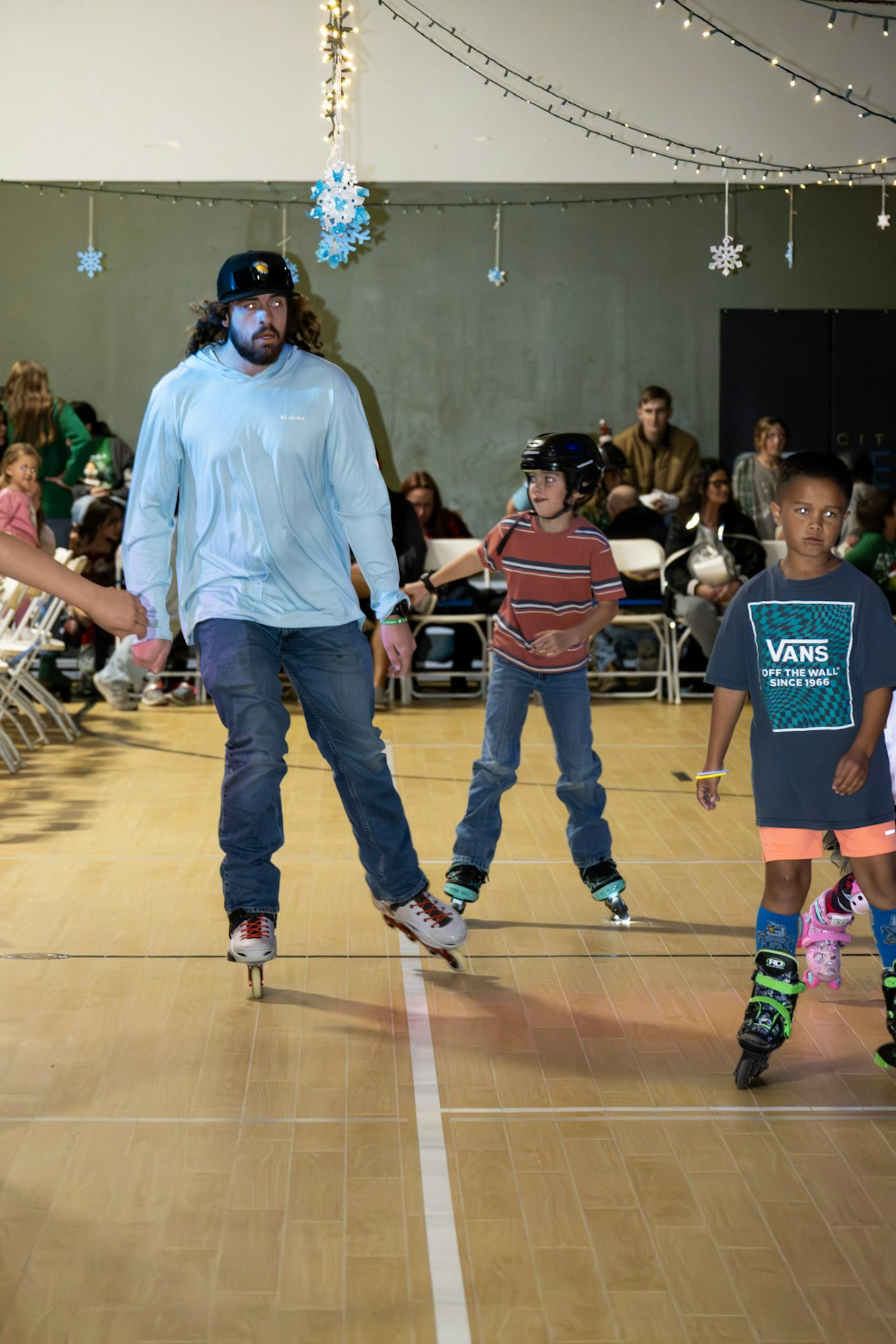 A group of children and an adult are roller skating indoors, with festive decorations overhead.
