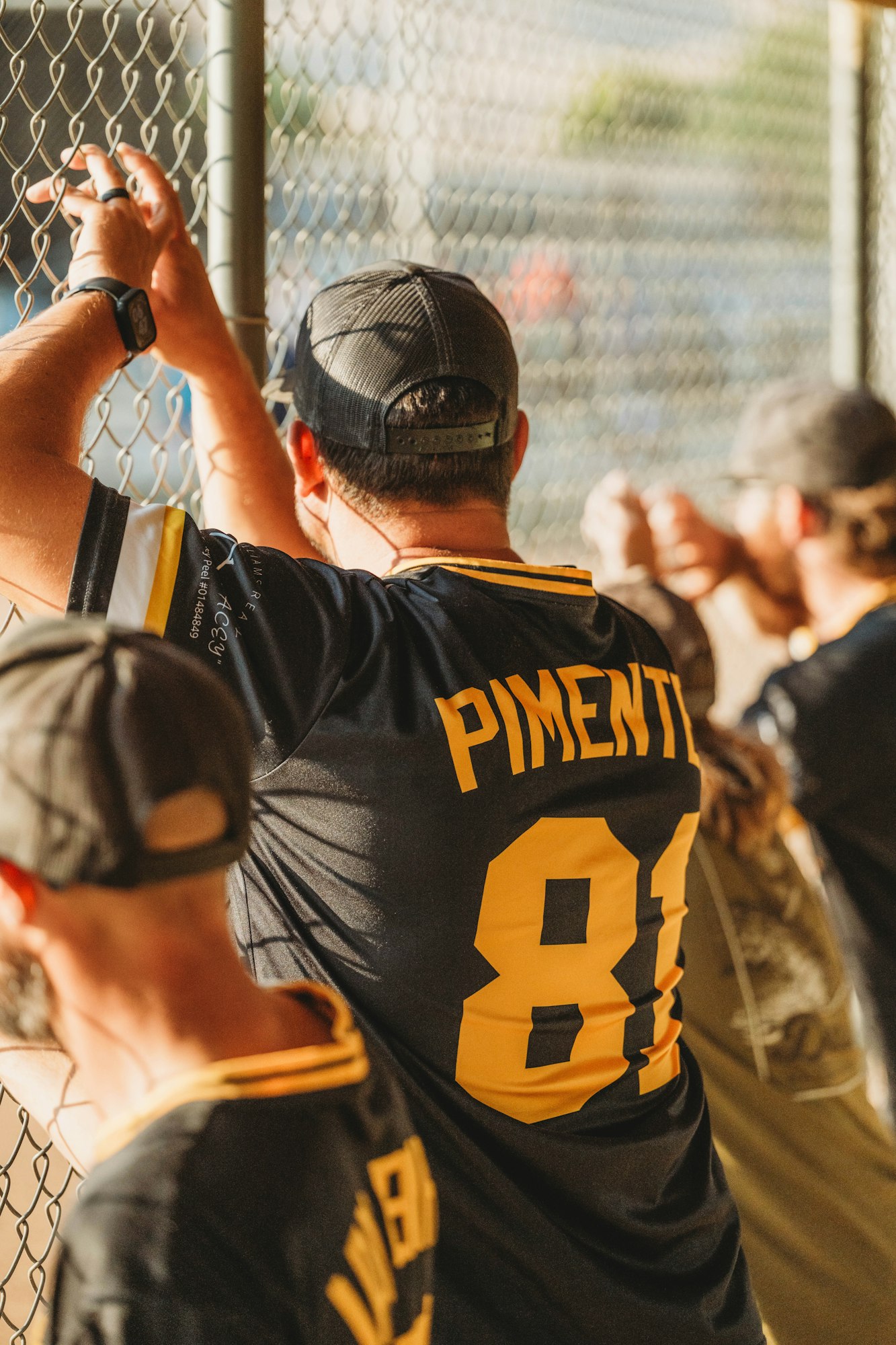 People watching a sports event behind a fence, wearing jerseys.