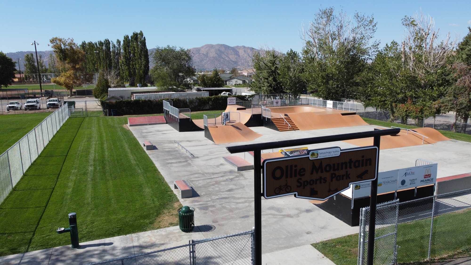 An aerial view of Ollie Mountain Sports Park featuring a skatepark, green grass, and nearby recreational areas.