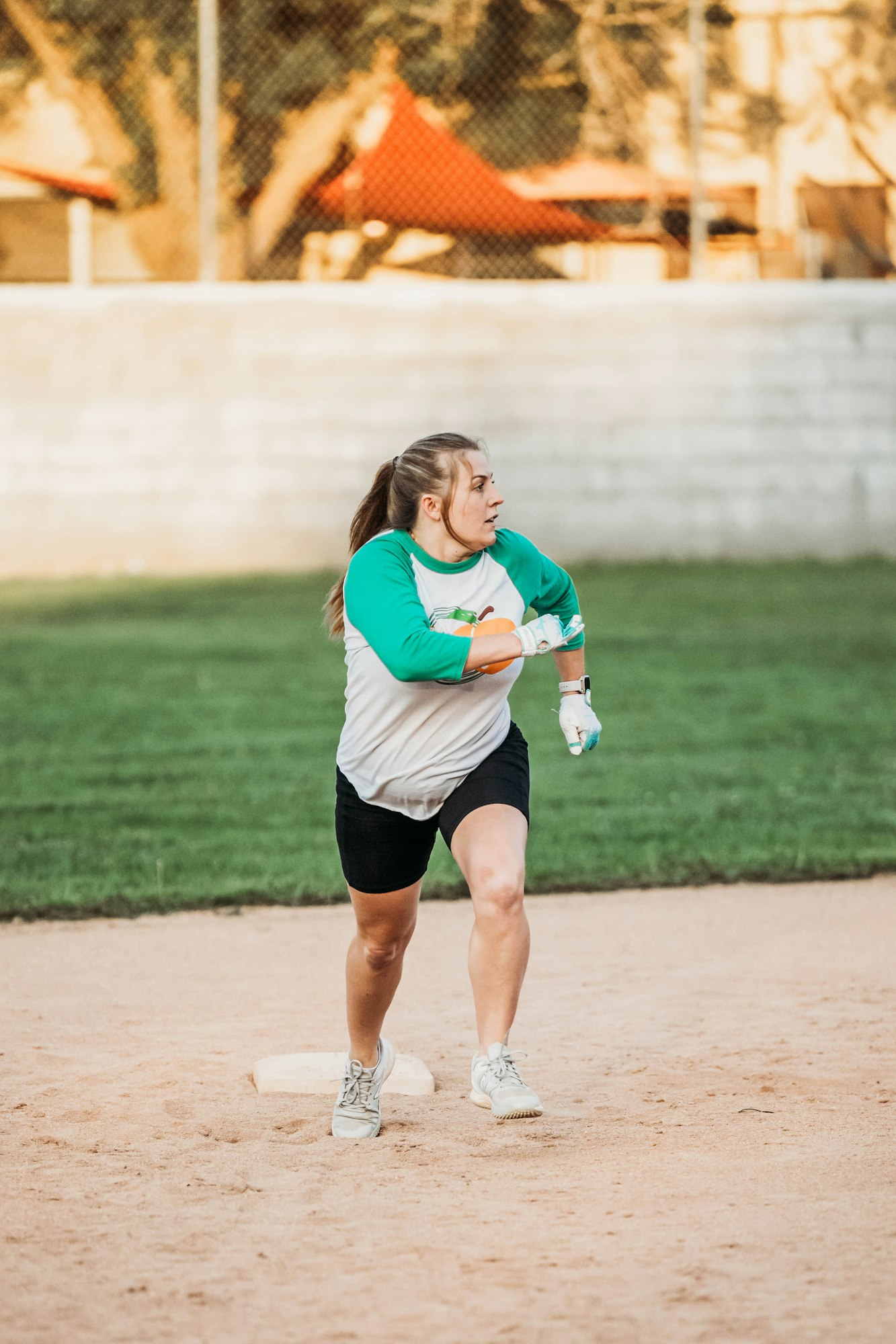 A focused woman playing softball, stepping on base.