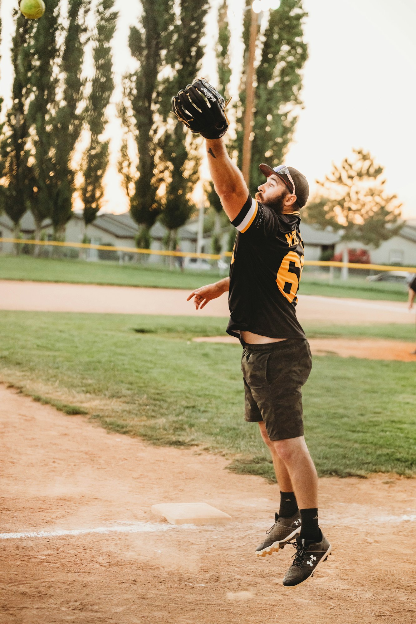 A man catching a softball in a park at dusk.