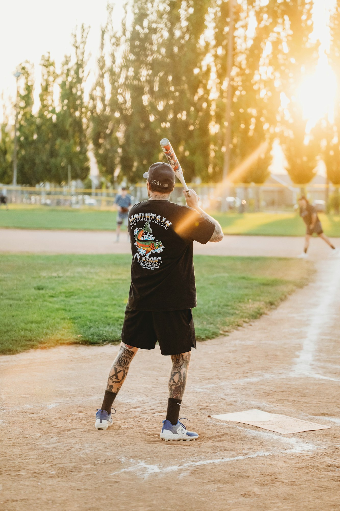 Person holding a baseball bat on a field, sunset in the background.