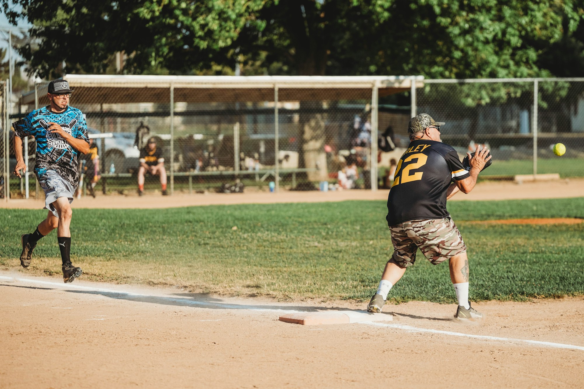 Two players in motion on a sunny softball field: one running to base, the other preparing to catch the ball.