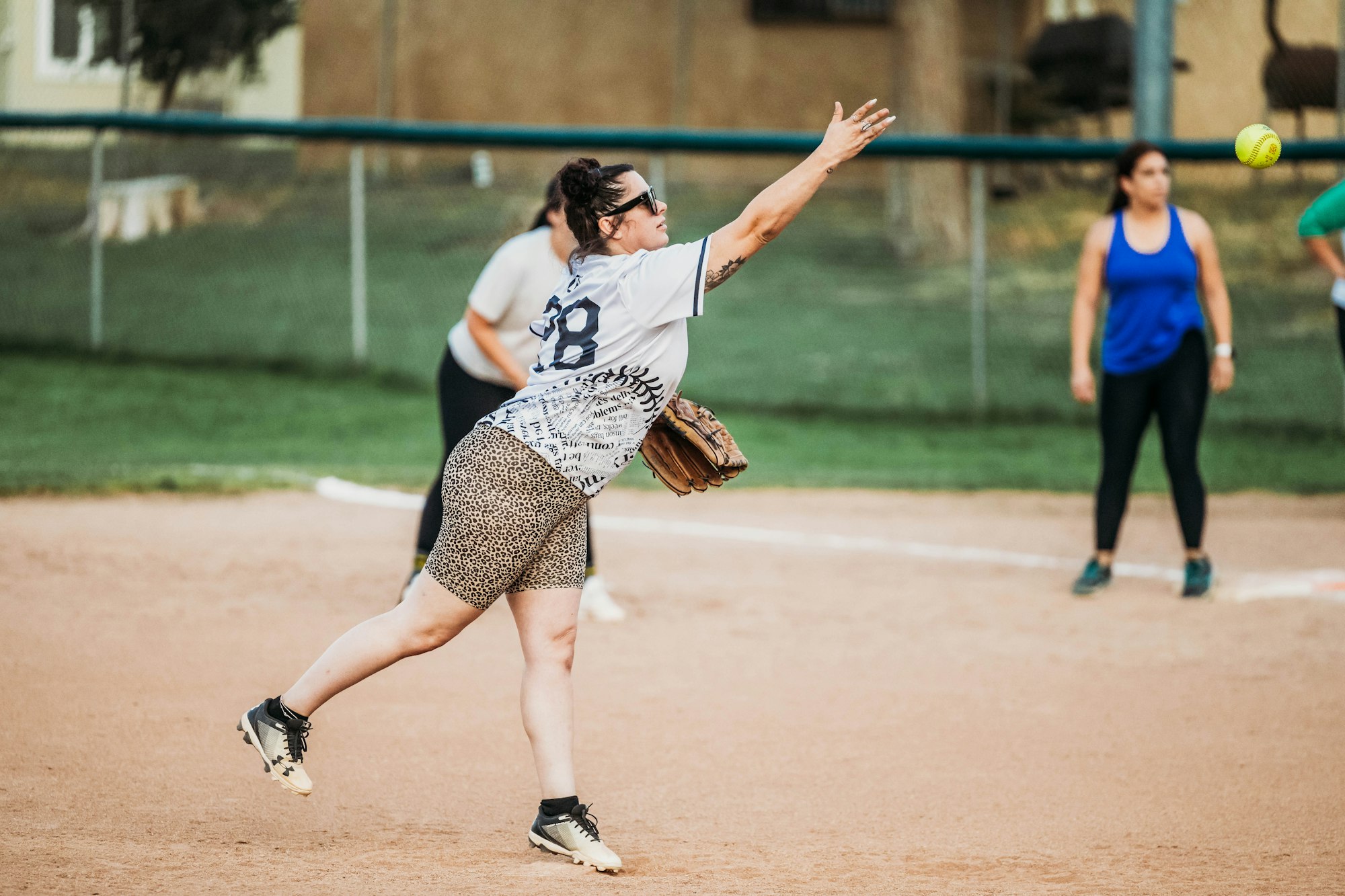 A softball player pitches the ball with teammates in the background.