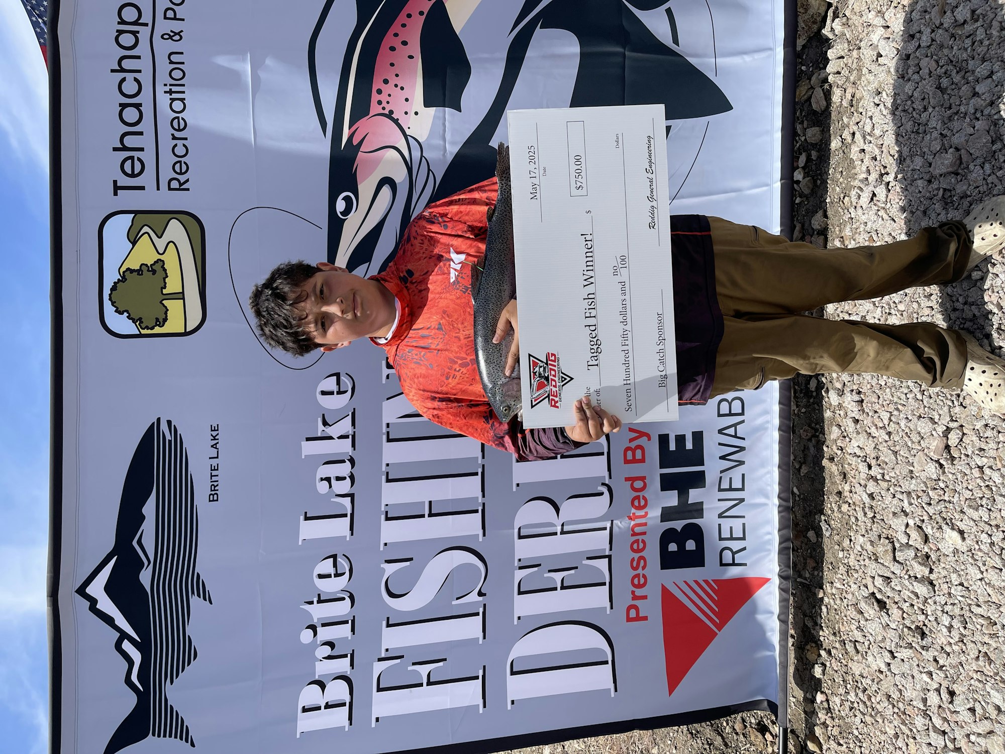 Person holding a large check at the Brite Lake Fishing Derby with a banner in the background.