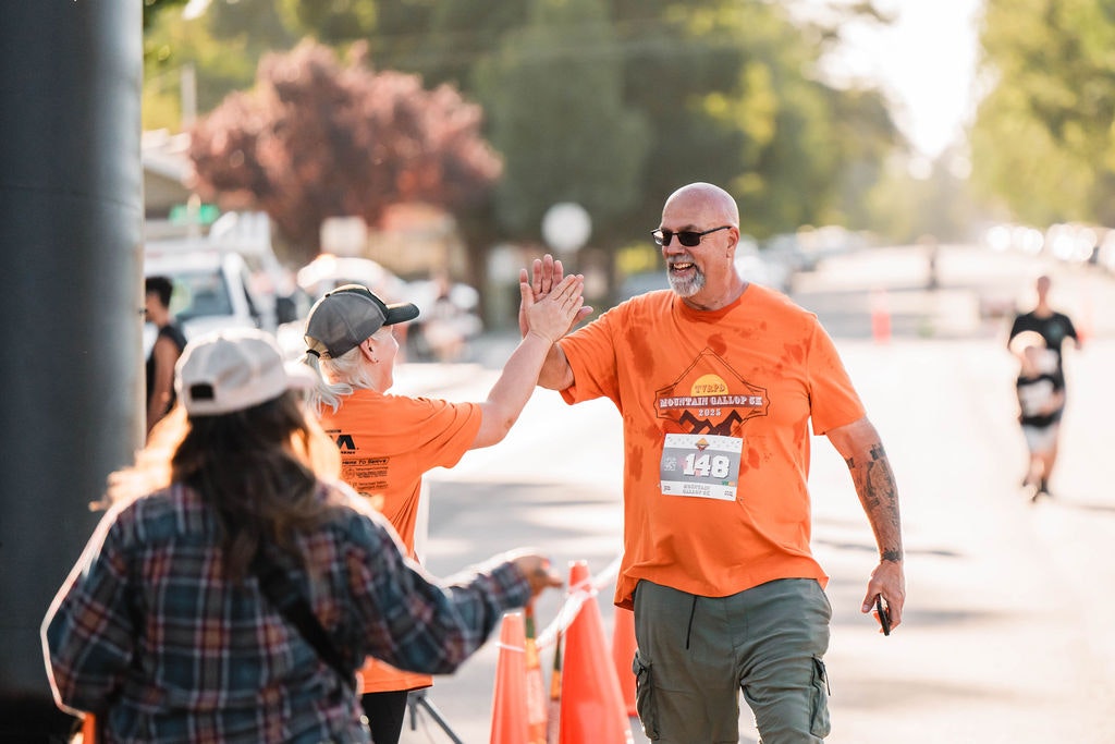 Two people in matching orange shirts high-fiving at an outdoor event.