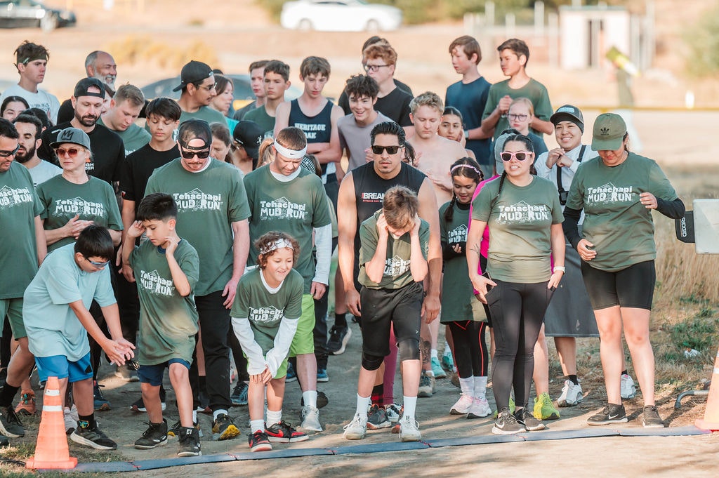 A group of people at the start of a mud run event, wearing matching shirts.