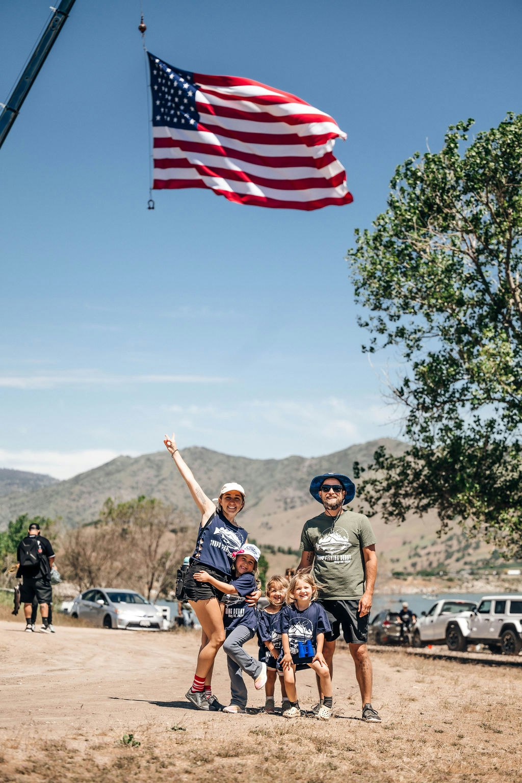 A family posing outdoors with an American flag waving in the background.