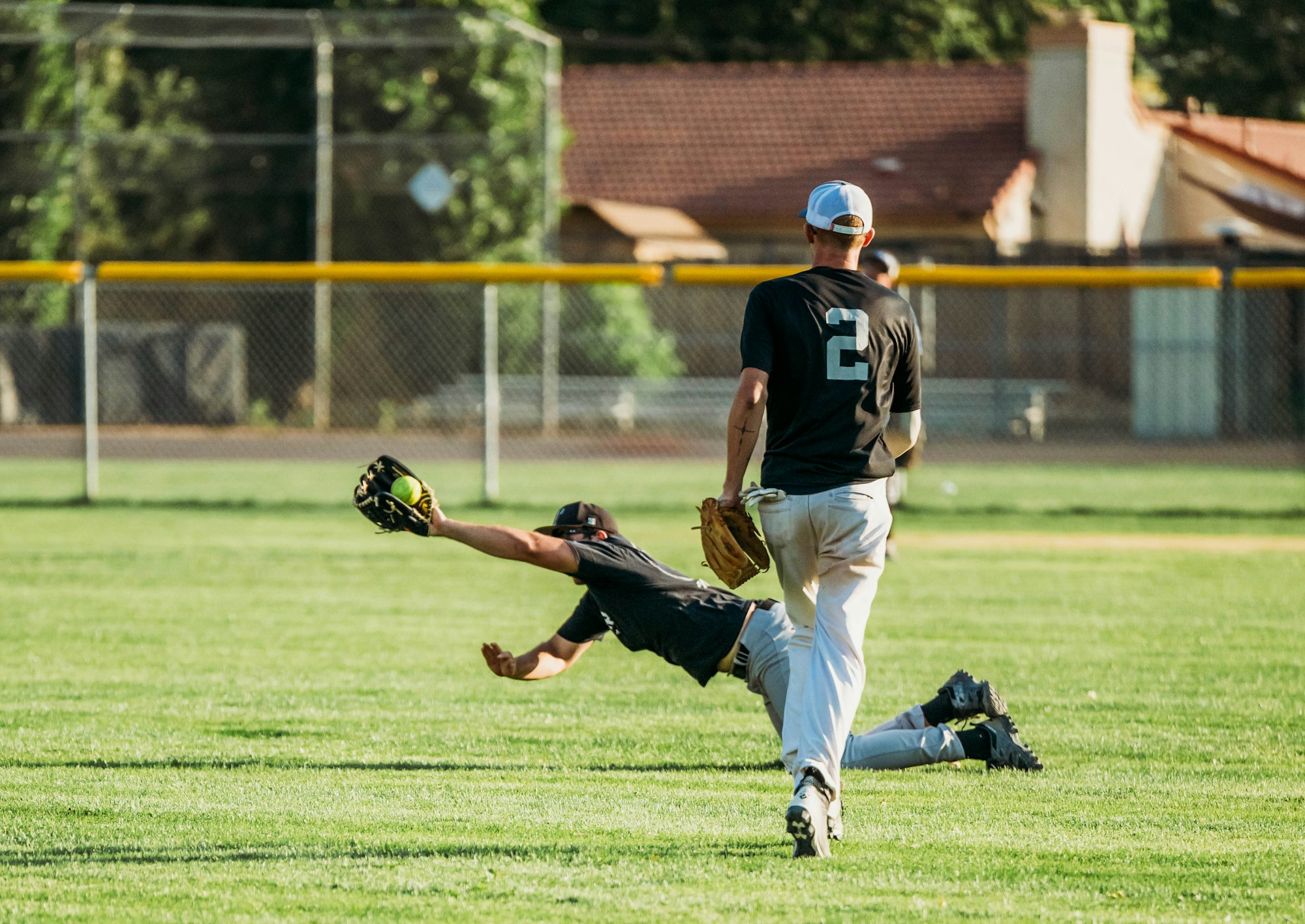 A baseball player diving to catch a ball while another player watches.