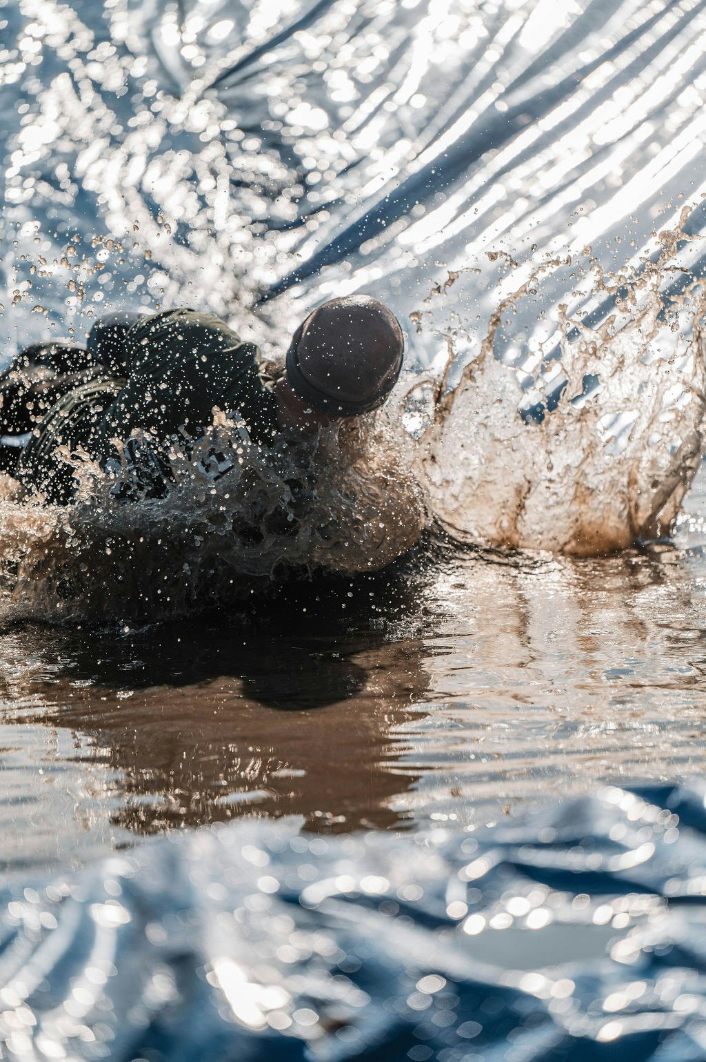 Person sliding down a water slide, creating splashes in the sunlight.