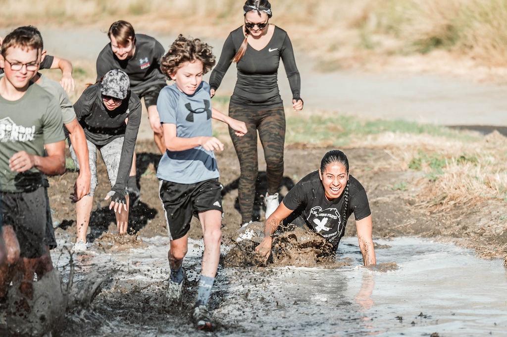 A group of people running and crawling through a muddy obstacle course, smiling and enjoying the challenge.