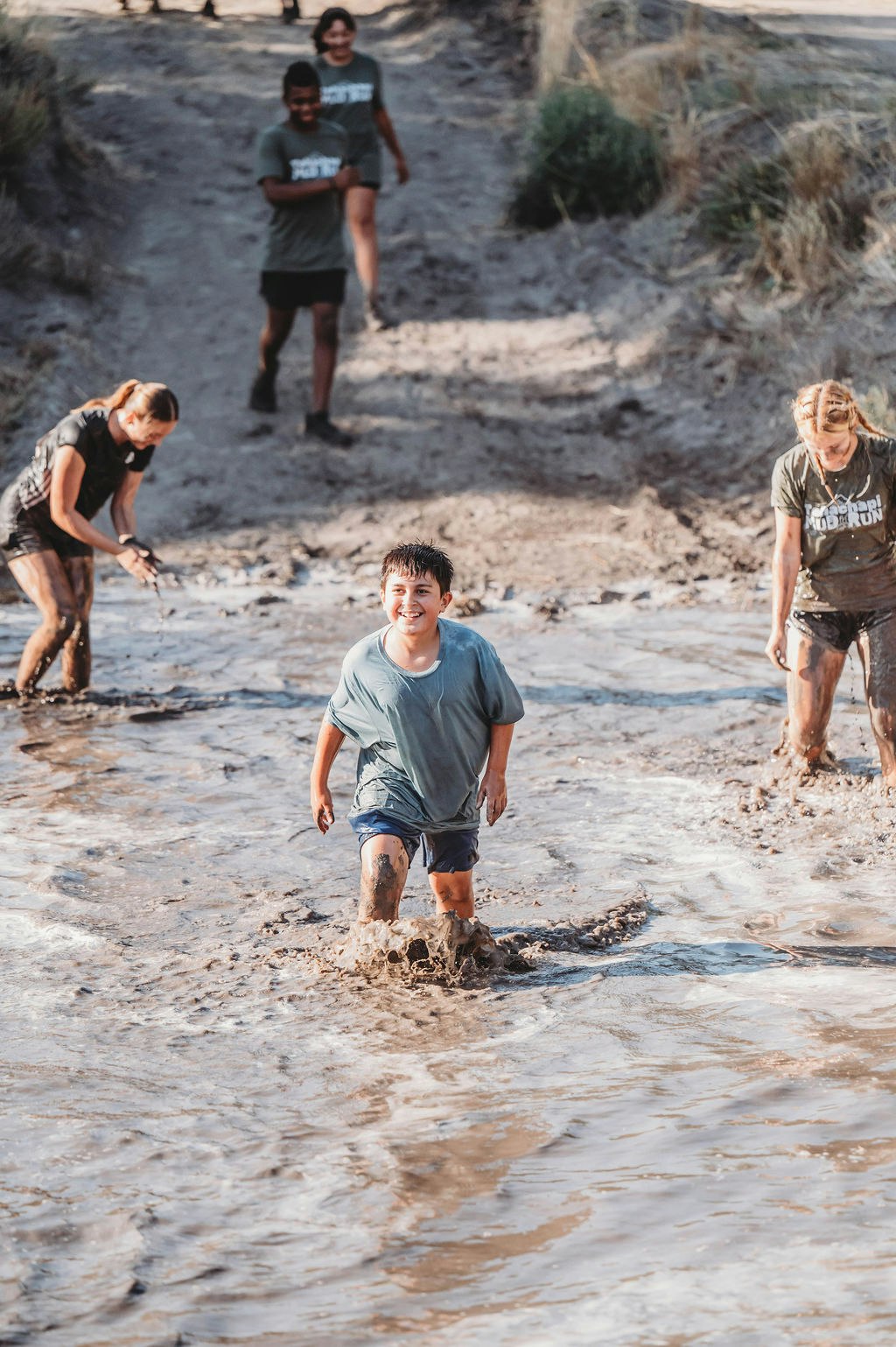 People running through a muddy water path, smiling and having fun.