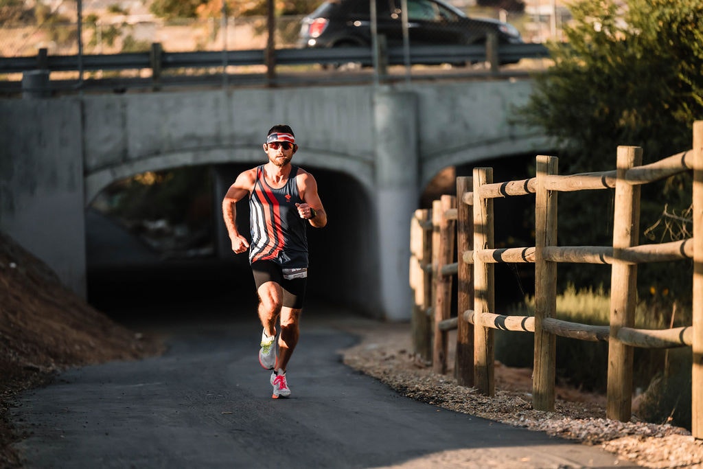A person running on a paved path under a bridge, with a wooden fence on the right.