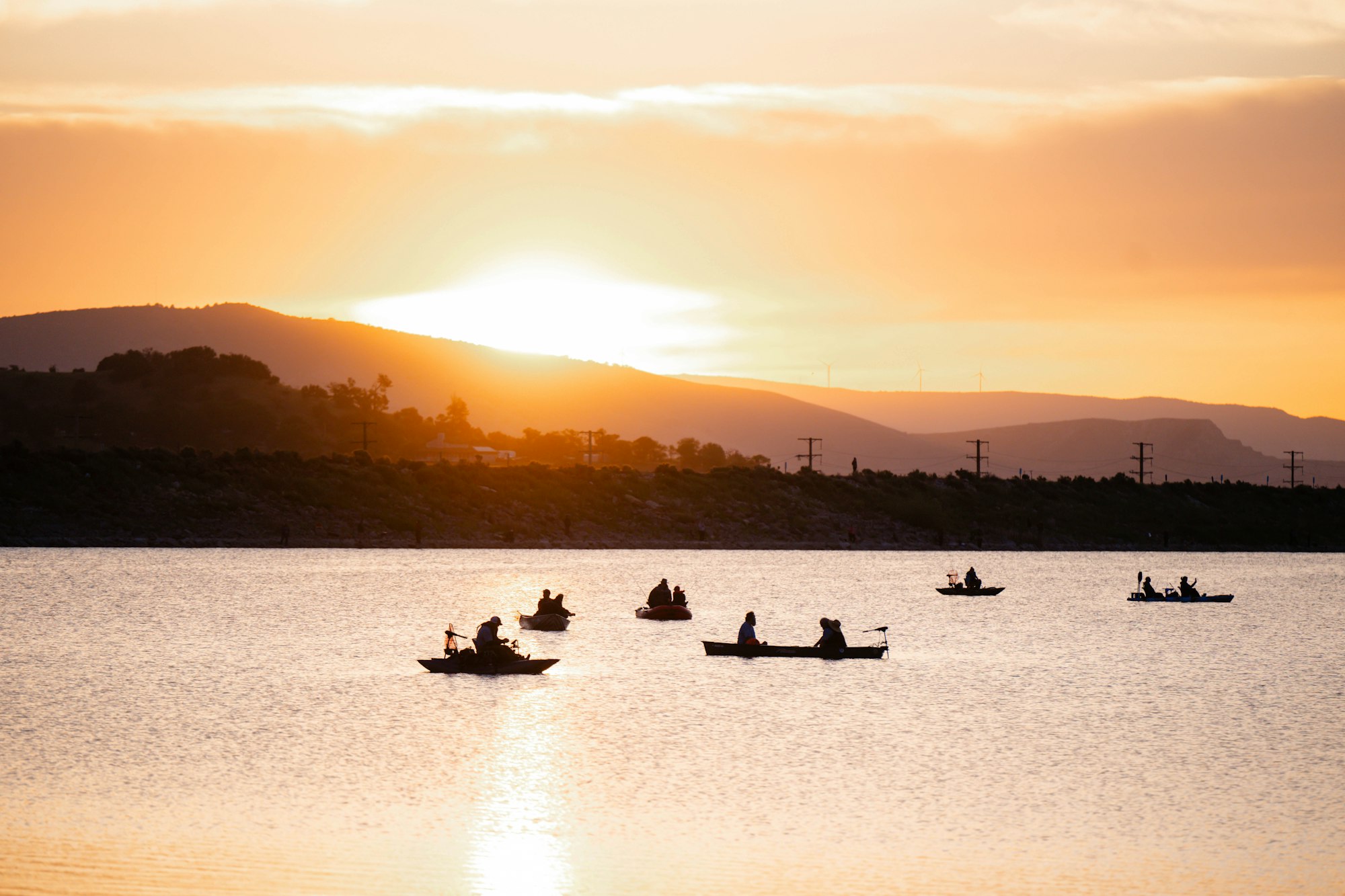 Kayakers on a calm lake at sunset, with hills silhouetted against an orange sky.