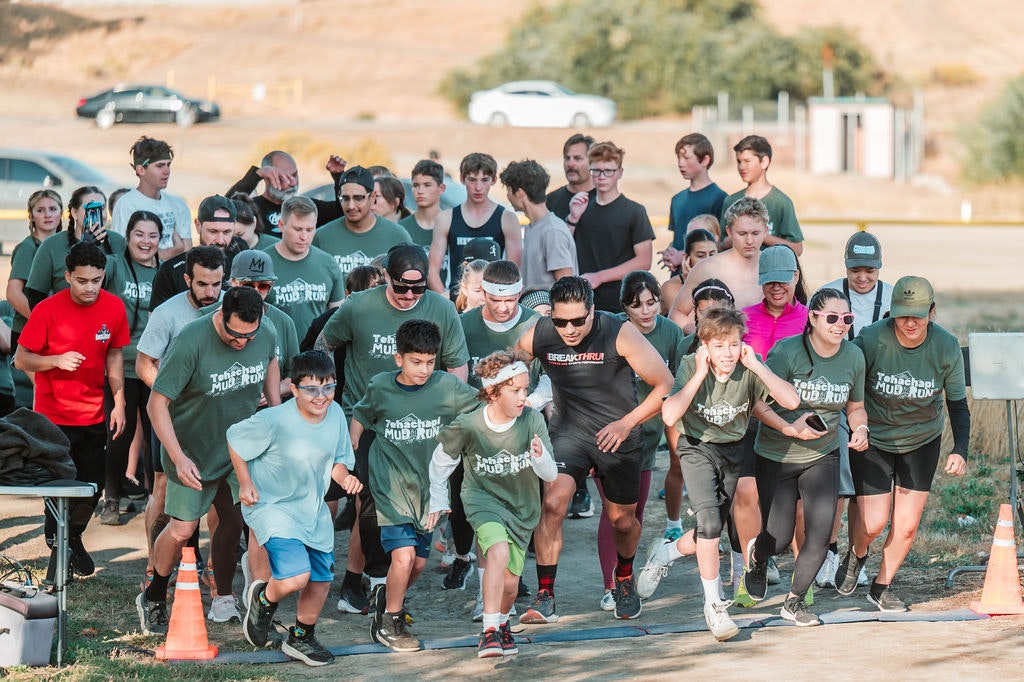 A group of people, mostly in green shirts, are starting a race at an outdoor event.