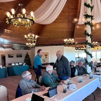 A group of people at a table in a decorated room with chandeliers and drapery, likely having a meeting or gathering.
