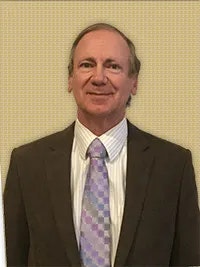 A person in a suit with a patterned tie, smiling against a plain background.