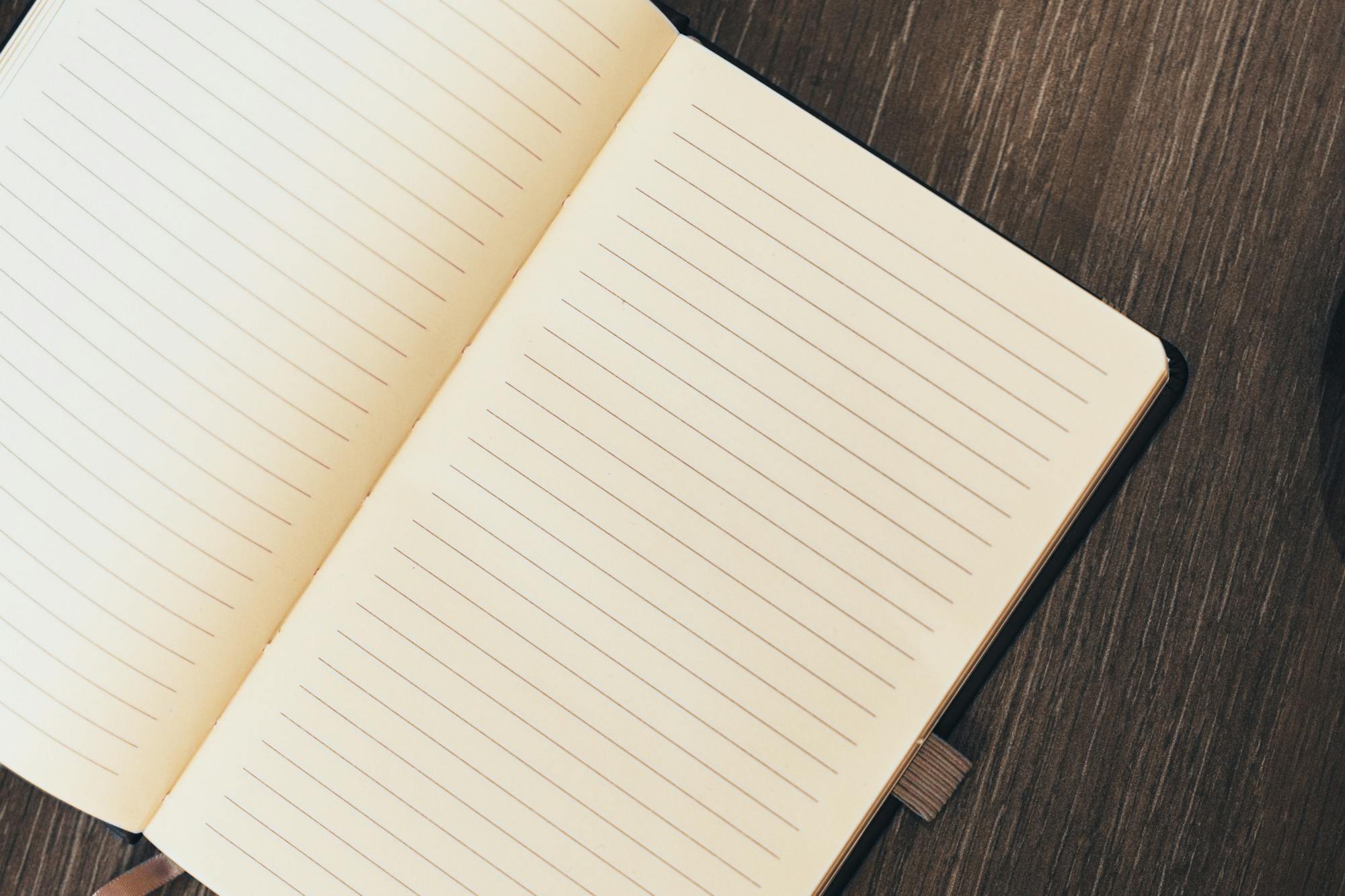 An open lined notebook rests on a wooden surface beside a cup of dark liquid, likely coffee or tea.
