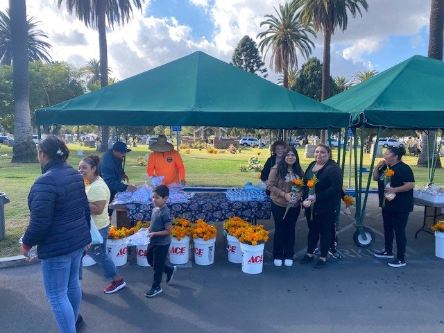 Photo contains people and flowers under a tent