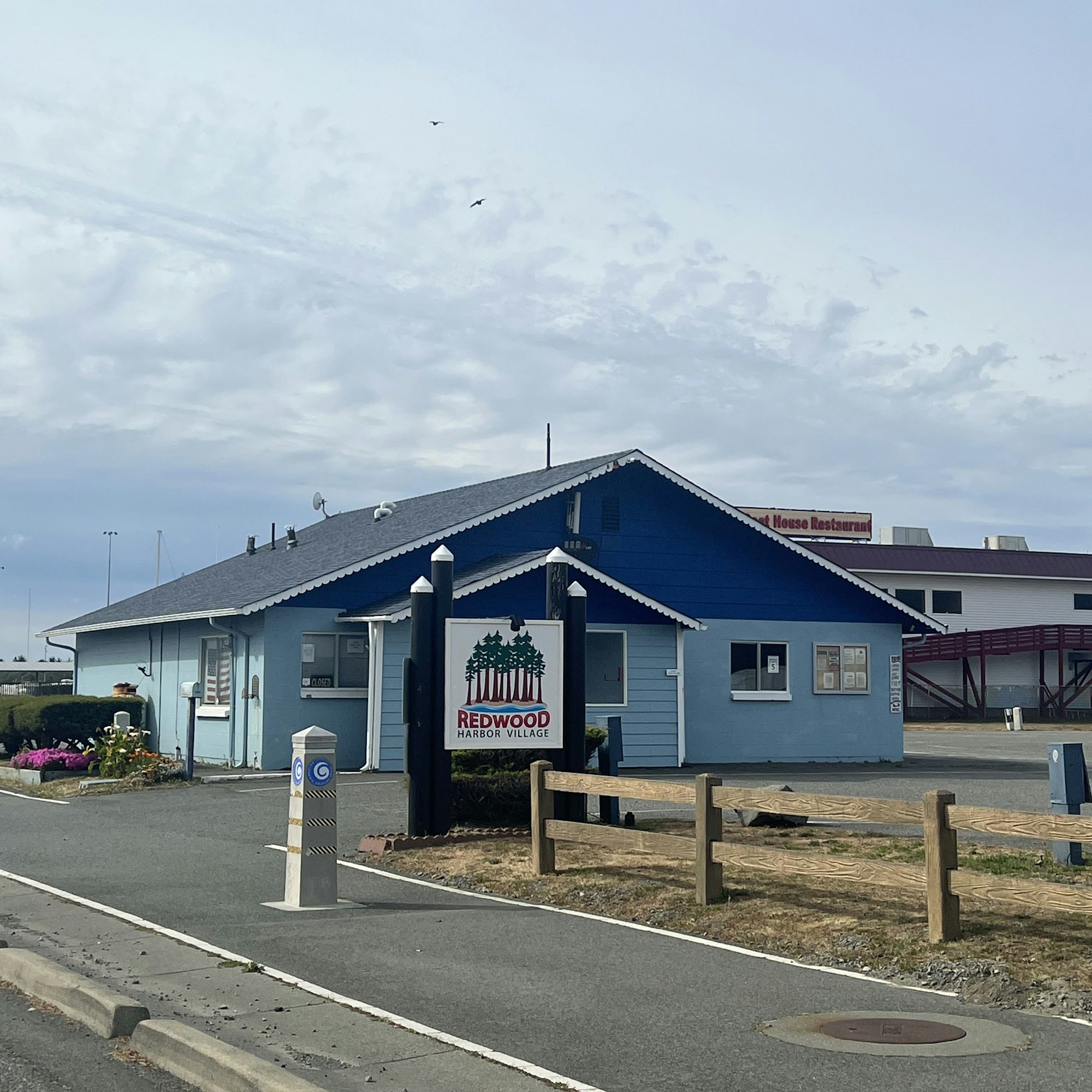 A blue building with a sign for "Redwood Harbor Village" and another sign indicating a restaurant nearby.