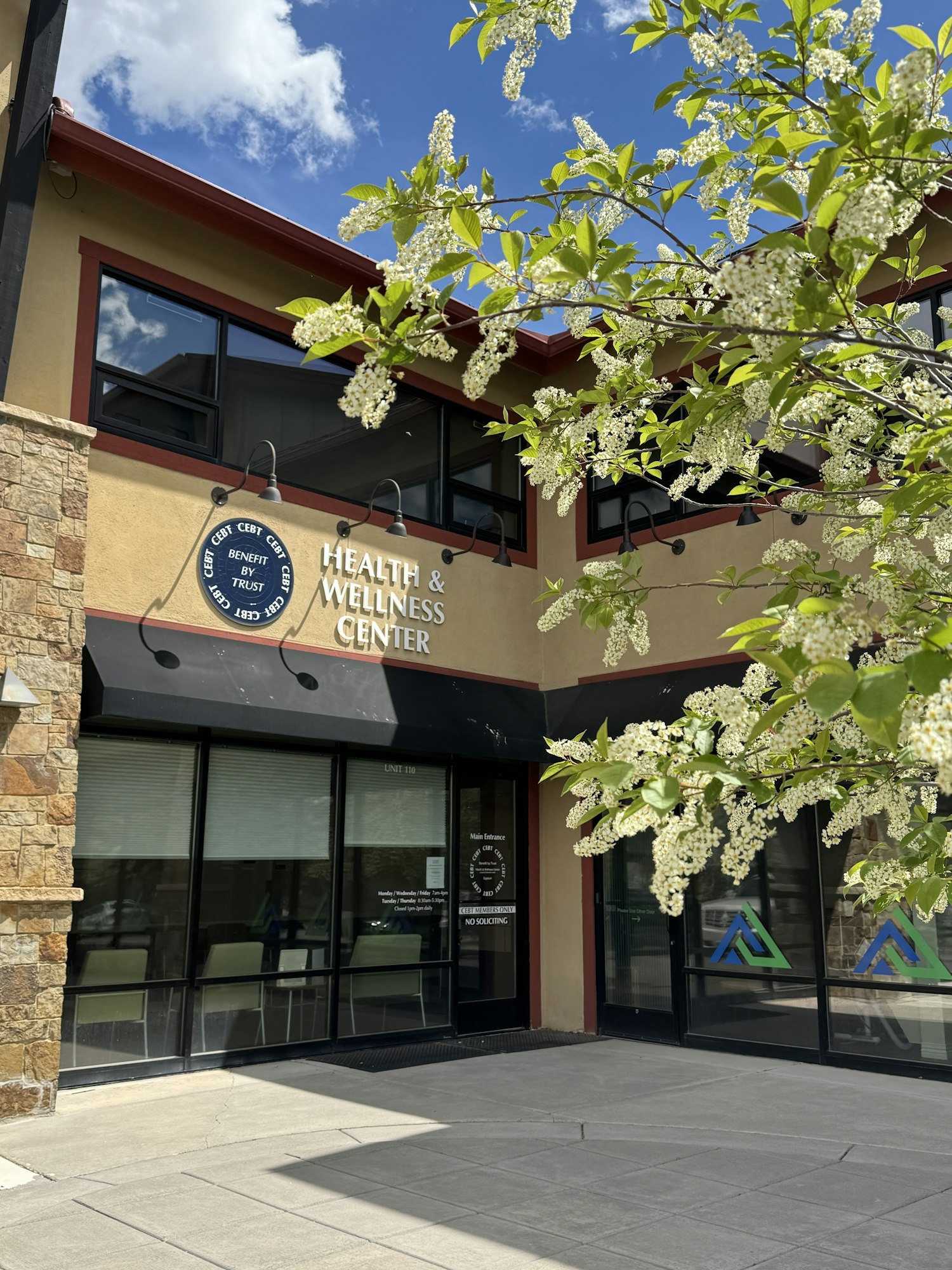 A building with a sign reading "Health & Wellness Center," surrounded by flowering trees and under a blue sky.
