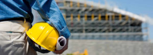 Photo of a worker holding helmet in front of a work site